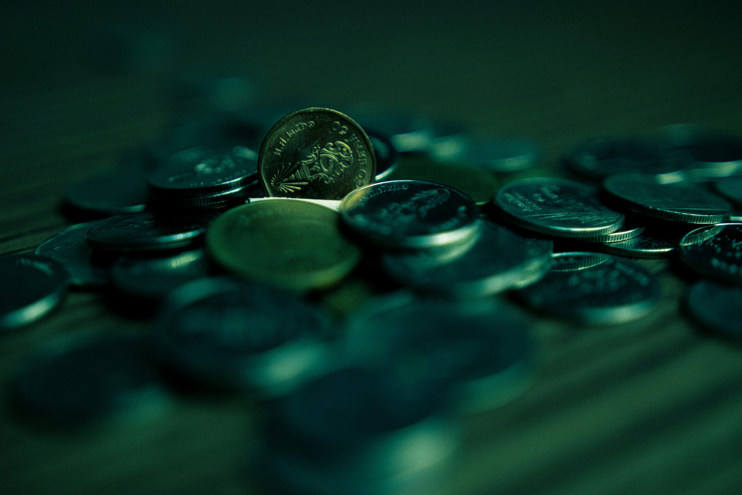 A collection of coins in varying sizes and shades of dark green, blending into a similarly colored background, evoking the easy-to-overlook costs that stem from poorly constructed RFPs.