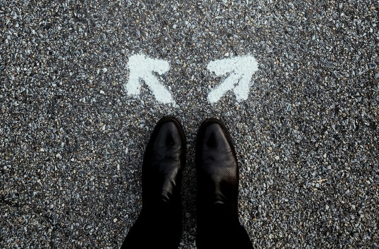 A pair of feet standing on asphalt between two painted arrows pointing in opposite directions—illustrating how strategic ambiguity in an RFP can invite interpretation while still guiding informed responses.