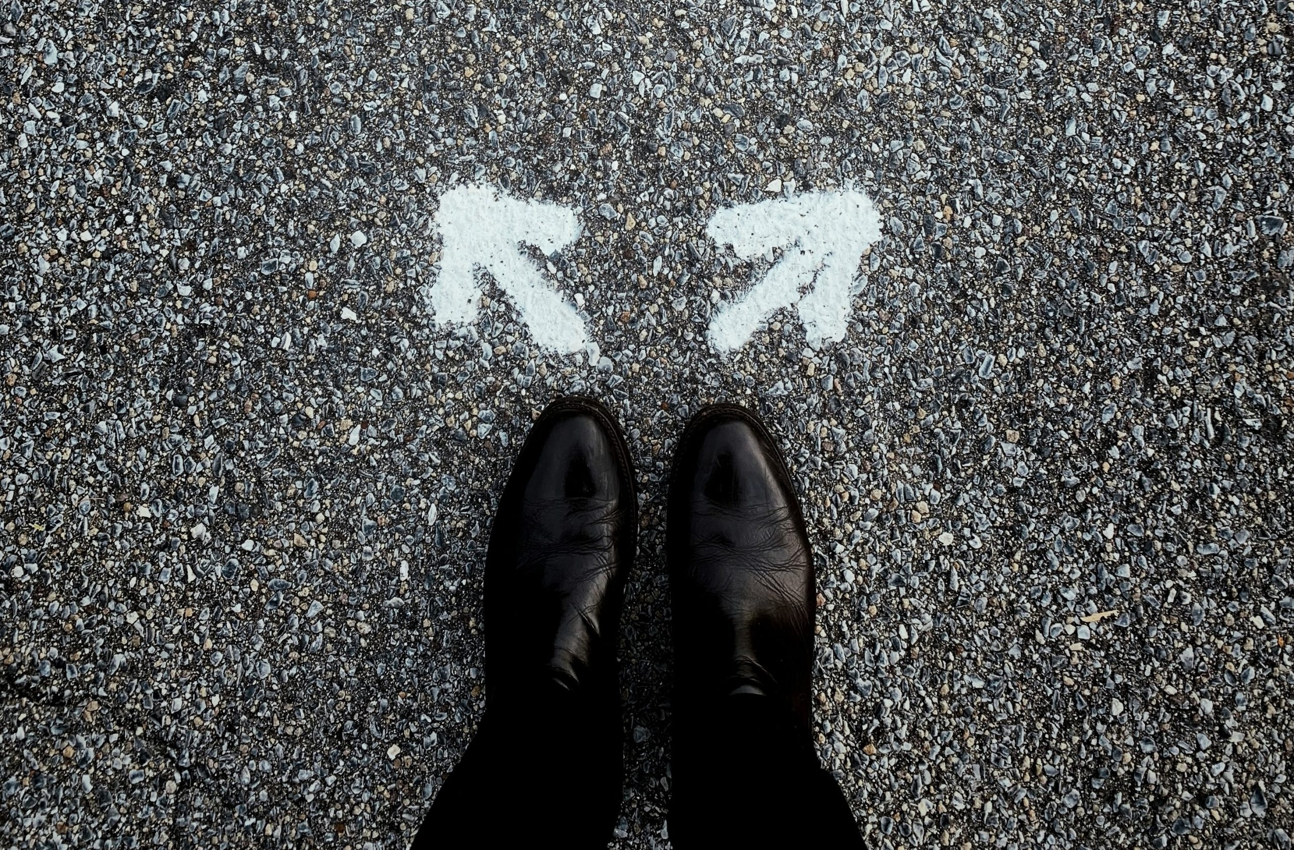 A pair of feet standing on asphalt between two painted arrows pointing in opposite directions—illustrating how strategic ambiguity in an RFP can invite interpretation while still guiding informed responses.