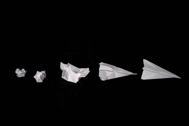 Sheets of paper from crumpled to paper plane on a black background, representing the strategist’s role in shaping and refining ideas with clarity and purpose.