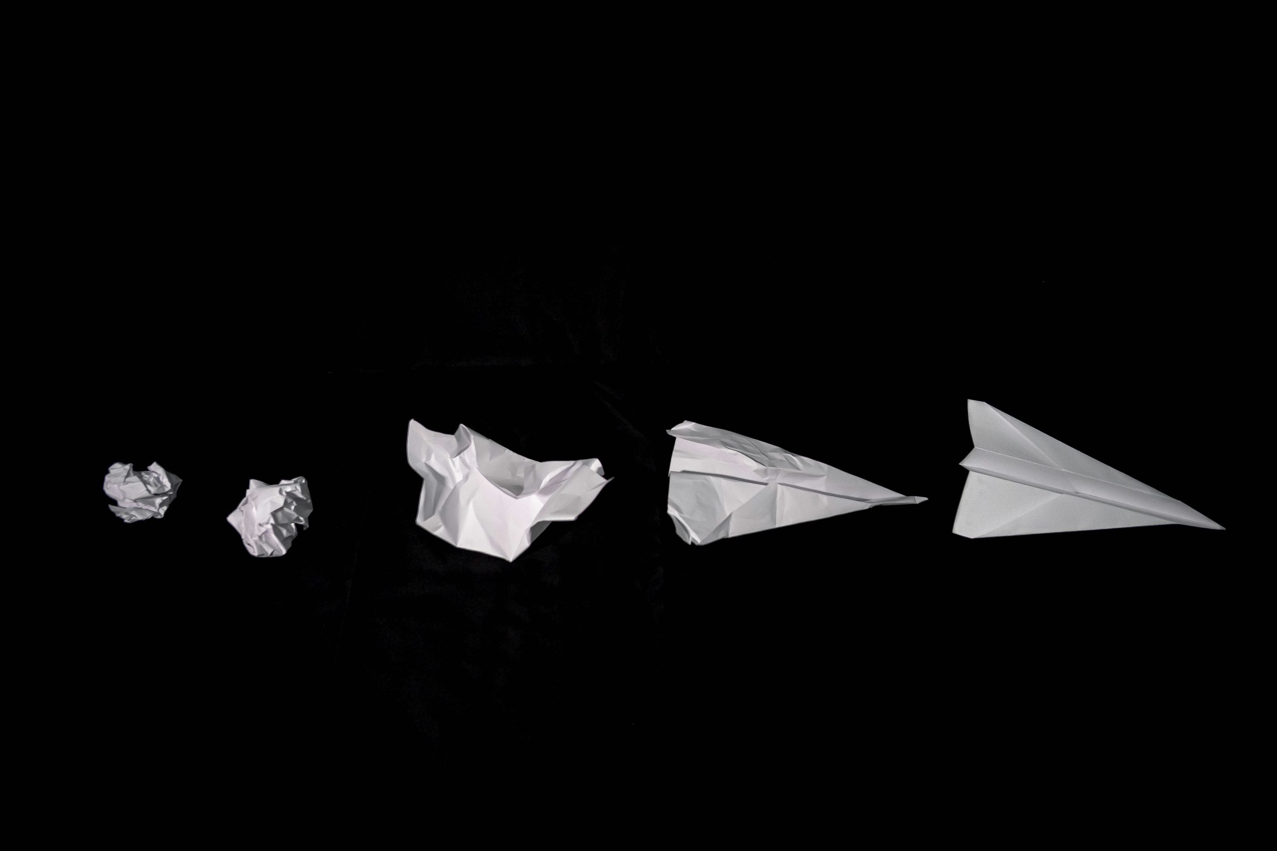 Sheets of paper from crumpled to paper plane on a black background, representing the strategist’s role in shaping and refining ideas with clarity and purpose.