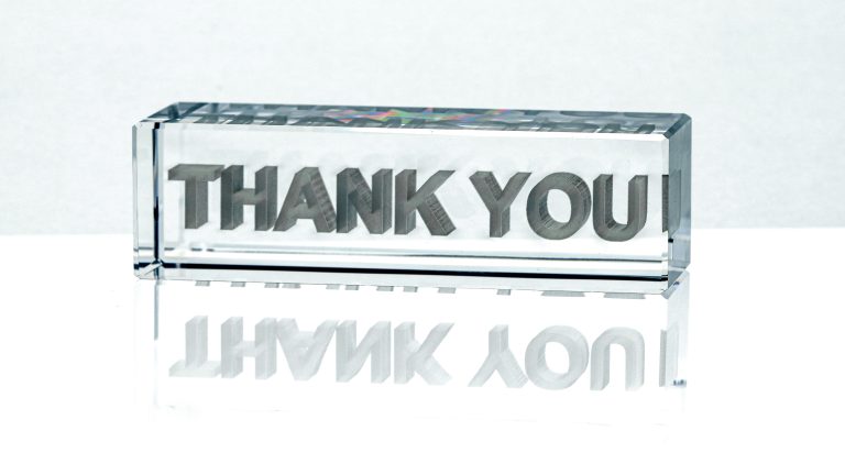 A glass block etched with the words “thank you,” reflected on a polished surface—symbolizing the lasting impact of thoughtful feedback and the value of closing the loop with respect and clarity.