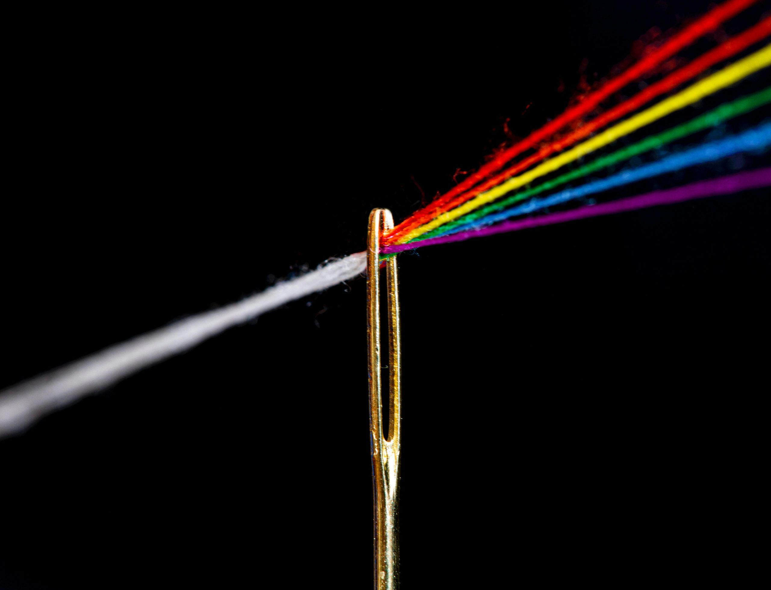 Colored threads converging through the eye of a needle, symbolizing strategic focus and clarity of direction.